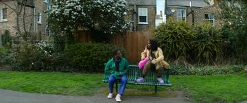 Rye Lane_Dom and Yas sit on a bench in the park
