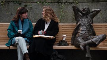 Singles_Linda and Ruth chat on a bench next top the sculpture